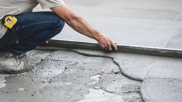 Construction worker leveling wet concrete floor using a metal screed tool