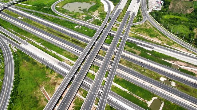 Aerial footage of a modern highway interchange stretching through a green rural landscape, The scale structure and flow of a major transportation infrastructure