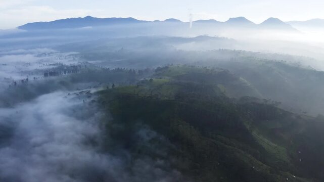 Stunning aerial view of rolling green hills covered in morning mist and low clouds against a mountain background.