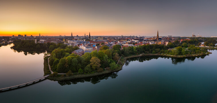 Panoramic aerial view capturing the Kobenhavn city skyline and park islands beautifully reflecting in tranquil lake waters during sunset light in Copenhagen, Denmark.