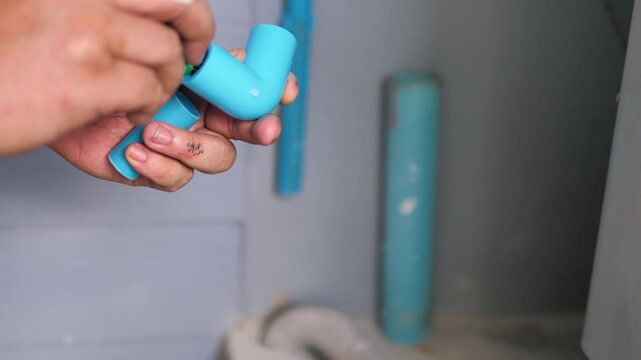 Close up of connecting a corner PVC pipe fitting by hand for DIY home plumbing repair and water system maintenance.