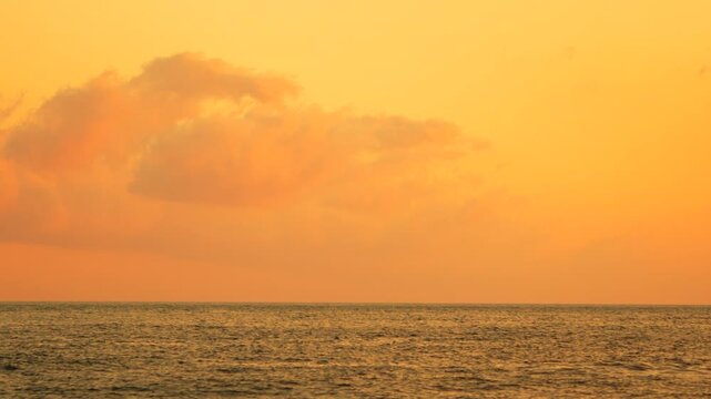 Sunset ocean horizon under a golden sky with soft clouds creating a peaceful atmosphere at dusk