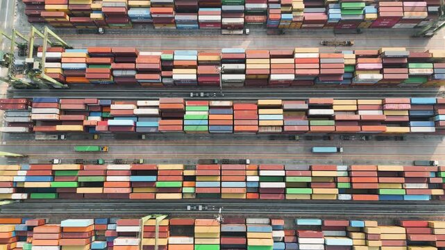 Top down aerial view of colorful shipping containers stacked in neat rows at a busy maritime logistics port terminal.