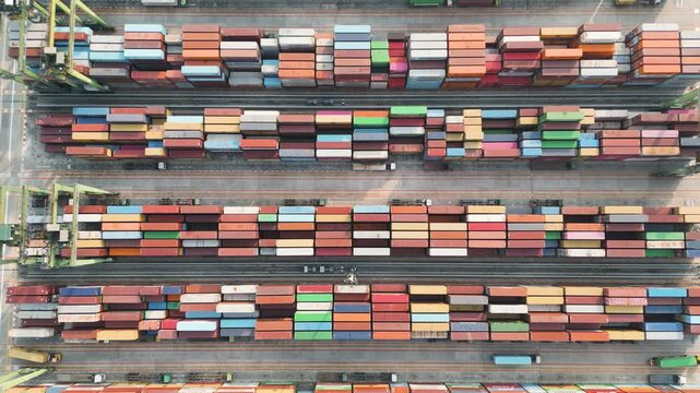 Aerial top down view of a busy shipping port terminal yard with stacked multi-colored cargo containers.