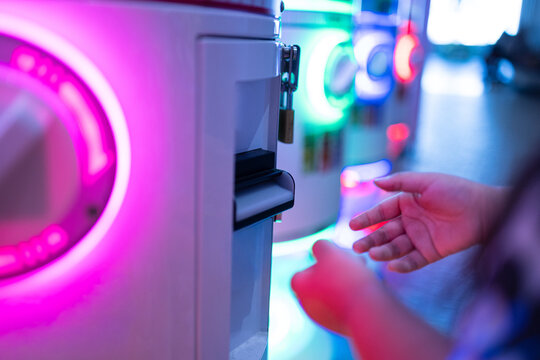 Neon Gachapon Vending Machine and Hand Interaction,A close-up of a person's hand reaching towards a vibrant, neon-lit capsule toy vending machine, capturing the excitement of modern Japanese-style gam