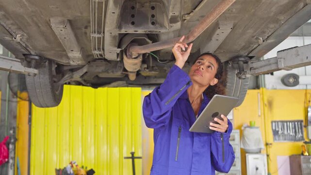 Automotive technician examining vehicle underside using tablet in a workshop setting