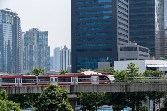 An LRT Jabodebek driverless train traveling on an elevated railway through Jakarta's modern Kuningan business district with skyscrapers in the background.