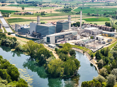 Aerial view of Centrale Termoelettrica - Moncalieri power plant situated along the Po River, surrounded by lush green fields and agricultural land in Moncalieri, Piemonte, Italy.