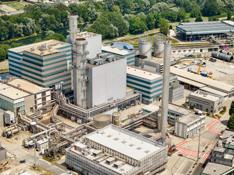 Aerial view of Centrale Termoelettrica Moncalieri power plant with tall chimneys, industrial buildings, and complex pipe networks near a river in Moncalieri, Piemonte, Italy.