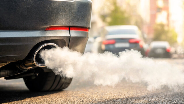 Closeup of a car exhaust pipe emitting thick white smoke on a city street