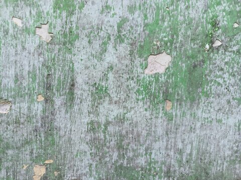 The rough, weathered texture of an old concrete wall. Its surface is uneven, featuring dark patches and mineral stains that reflect the natural aging process, along with peeling paint.