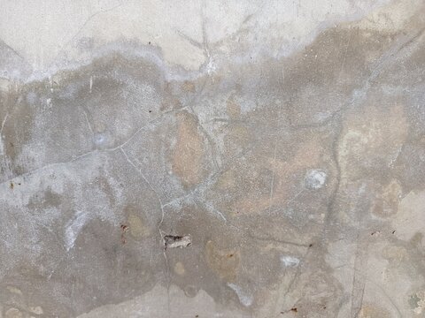 A close-up shot captures the rough, weathered texture of an old concrete wall. The surface is uneven, dark patches, mineral stains, and reflecting natural aging