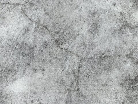 A close-up shot captures the rough, weathered texture of an old concrete wall. The surface is uneven, dark patches, mineral stains, and reflecting natural aging