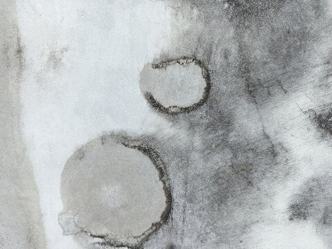 A close-up shot captures the rough, weathered texture of an old concrete wall. The surface is uneven, dark patches, mineral stains, and reflecting natural aging