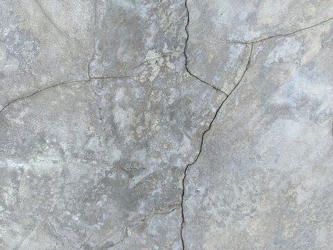 A close-up shot captures the rough, weathered texture of an old concrete wall. The surface is uneven, dark patches, mineral stains, and reflecting natural aging