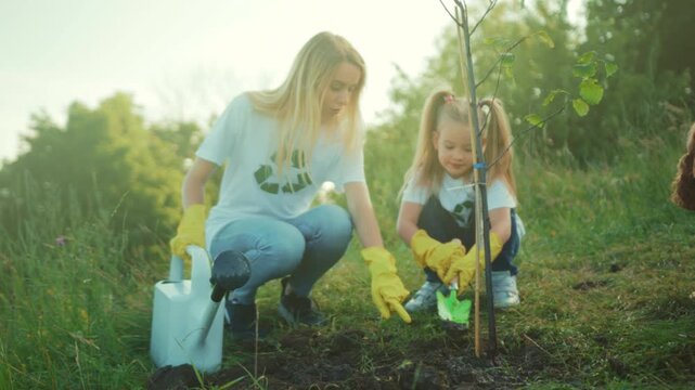Mother and daughter nurture tree outdoors, Mother and daughter jointly cultivate sapling in sunny field while bonding