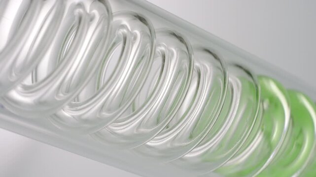 Pale green transparent fluid flowing through the spiral of an inclined coil laboratory condenser, filling it up on grey background | Centella asiatica infusion cosmetic base ingredient concept