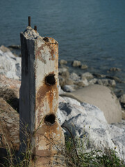 Fototapeta premium Rusted iron bars are attached to weathered concrete pillars along the seashore the exposed metal rebar is corroded by the salty air set against a backdrop of a green sea.