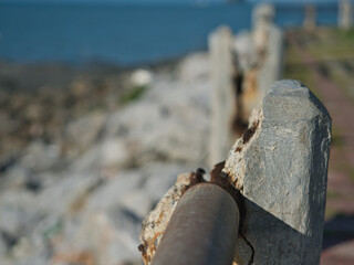 Naklejka premium Rusted iron bars are attached to weathered concrete pillars along the seashore the exposed metal rebar is corroded by the salty air set against a backdrop of a green sea.