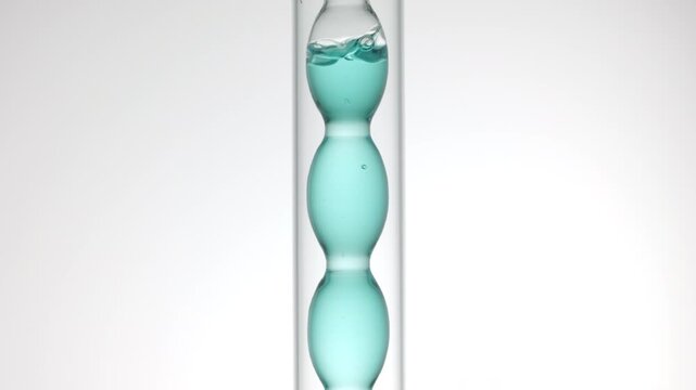 Magnified view of air bubbles rushing through pale cyan transparent liquid as it fills and drains from a bulb laboratory condenser over soft gray background | Cosmetic toner promotional concept