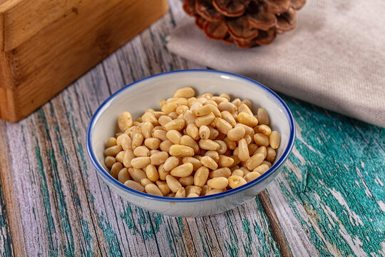 Organic pine nuts in a white ceramic bowl on a rustic distressed wooden table