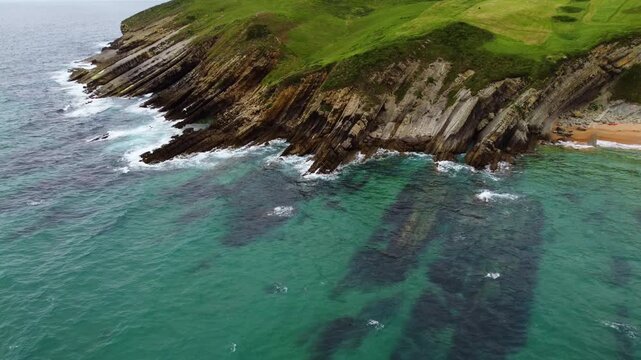 Dramatic aerial drone view of flysch rock formations and cliffs on the Cantabrian coast, Spain. Turquoise ocean waves crashing against unique geological strata. High quality 4k footage