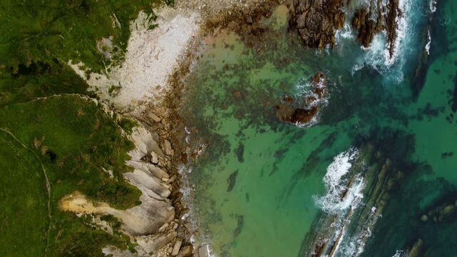 Top down aerial view of turquoise ocean waves crashing against a rocky coast. Natural abstract sea texture and background from above, Cantabria, Spain. High quality 4k footage