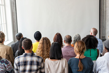 Obraz premium Diverse group of people seated, facing a blank presentation screen.