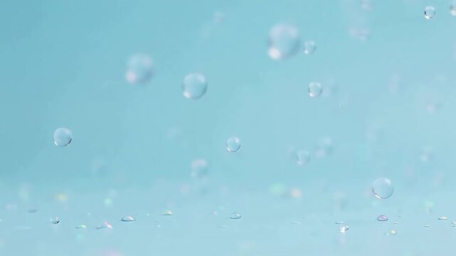 Water droplets falling against a soft blue background, creating a serene and reflective surface with subtle iridescent highlights.