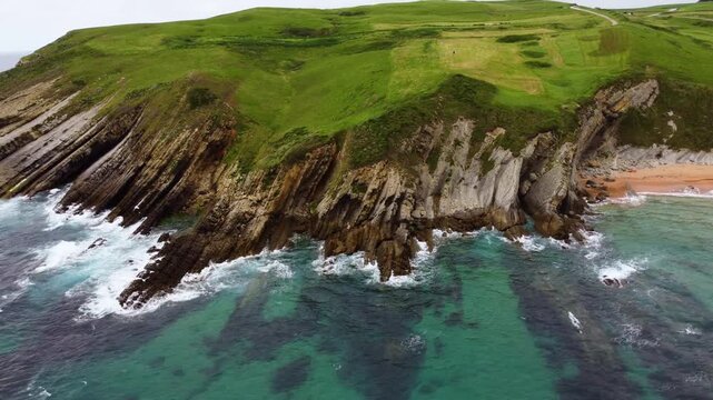 Dramatic aerial drone view of flysch rock formations and cliffs on the Cantabrian coast, Spain. Turquoise ocean waves crashing against unique geological strata. High quality 4k footage