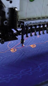 Industrial embroidery machine stitching decorative gold patterns on navy blue fabric