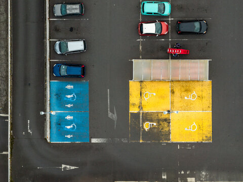 Aerial view of a parking lot featuring blue and yellow accessible parking spaces with painted symbols and parked cars in Angra do Heroismo, Azores, Portugal.