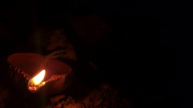 Traditional clay oil lamp diya burning with bright, steady flame in dark setting. Warm glow creates peaceful spiritual atmosphere, making it ideal for Diwali celebrations, Hindu worship, meditation