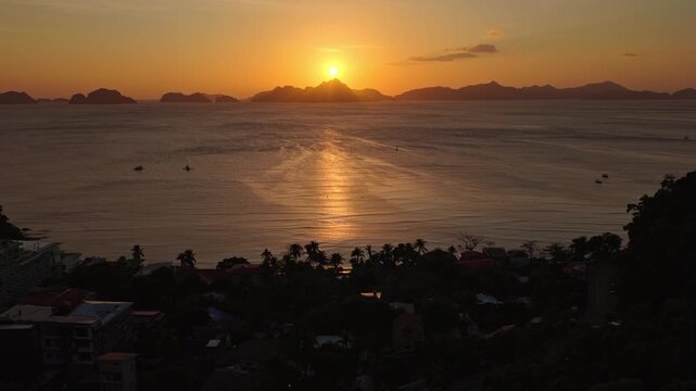 Aerial Sunset Panning Shot of Corong Corong Beach in El Nido, Philippines. Drone Right to Left Golden Hour View of Orange Sky and Sun Reflecting on Calm Ocean Water.