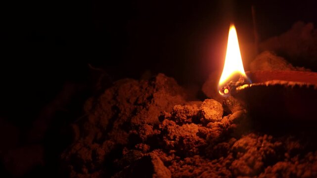 Traditional clay oil lamp diya burning with bright, steady flame in dark setting. Warm glow creates peaceful spiritual atmosphere, making it ideal for Diwali celebrations, Hindu worship, meditation