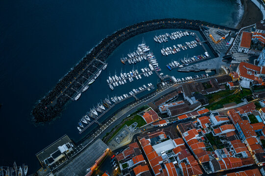 Aerial view of the marina in Angra do Heroismo with yachts moored in the harbor, protected by a stone breakwater, near historic town rooftops in Angra do Heroismo, Azores, Portugal.