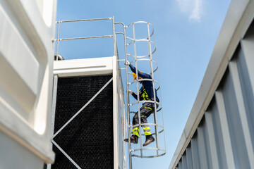 Technician man climbing a safety ladder to inspect industrial cooling system, Professional worker accessing HVAC equipment, Industrial maintenance worker in safety gear climbing a caged ladder © JU.STOCKER