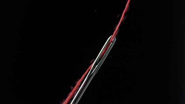 Macro sewing needle being threaded with red thread in dramatic closeup craft scene