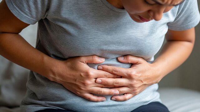 A close-up view of a person wearing a grey t-shirt, clutching their abdomen in obvious physical pain.