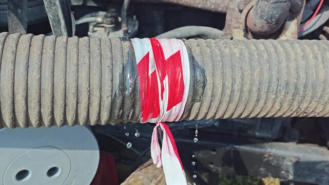 Close-up of a water leak from a ribbed rubber hose wrapped with red and white warning tape on a running machine.