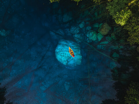 Aerial view of Danau Paisu Pok Luk Panenteng with a small boat floating on clear turquoise water surrounded by lush tropical vegetation in Bulagi Utara, Central Sulawesi, Indonesia.