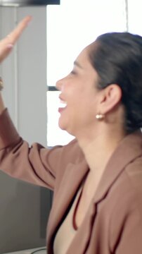 Vertical video: Entering hand spurring joy, woman in gray top with mug highfiving in office lounge