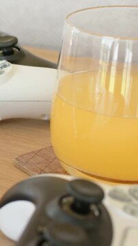 Vertical video: Panning handheld camera focusing on white gamepad and orange juice glass on table