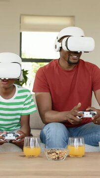 Vertical video: Playing at game start dad red tee son on sofa using VR gear, trying to win