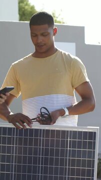 Vertical video: As coworker showing phone, man in yellow tee aligning MC4 plugs to connect in yard