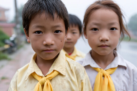 Three children wear yellow ties and light shirts. They stand outdoors with serious, curious expressions. One child stares directly at the camera, unblinking