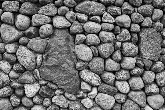 Black and white background texture of an old stone masonry wall built with natural round cobbles and rustic boulders.