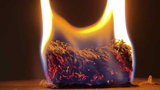 A small cluster of dry material burns with a vibrant golden flame. The bright light contrasts sharply with the deep black background. This simple fire creates a feeling of warmth and mystery.