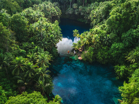 Aerial view of Danau Paisu Pok Luk Panenteng with its vibrant turquoise waters surrounded by dense tropical jungle and palm trees in Bulagi Utara, Central Sulawesi, Indonesia.