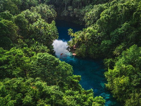 Aerial view of Danau Paisu Pok Luk Panenteng surrounded by dense tropical jungle with crystal clear blue water and a small boat in Bulagi Utara, Central Sulawesi, Indonesia.